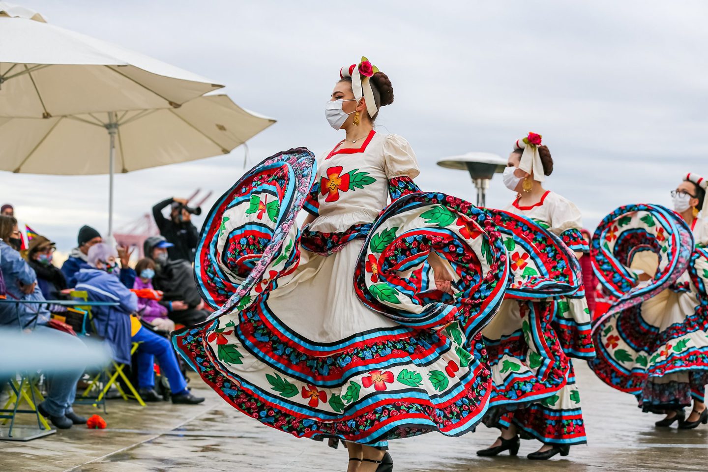 Women wearing white dresses with colorful hemming and embroidery dance.