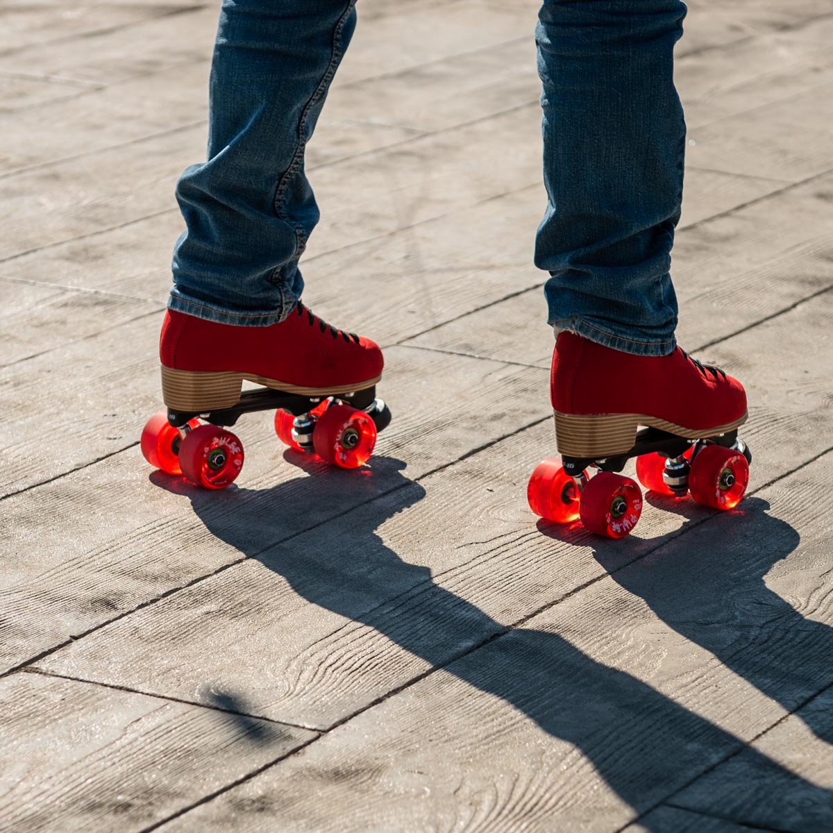 A pair of red roller skates with red wheels on a boardwalk.