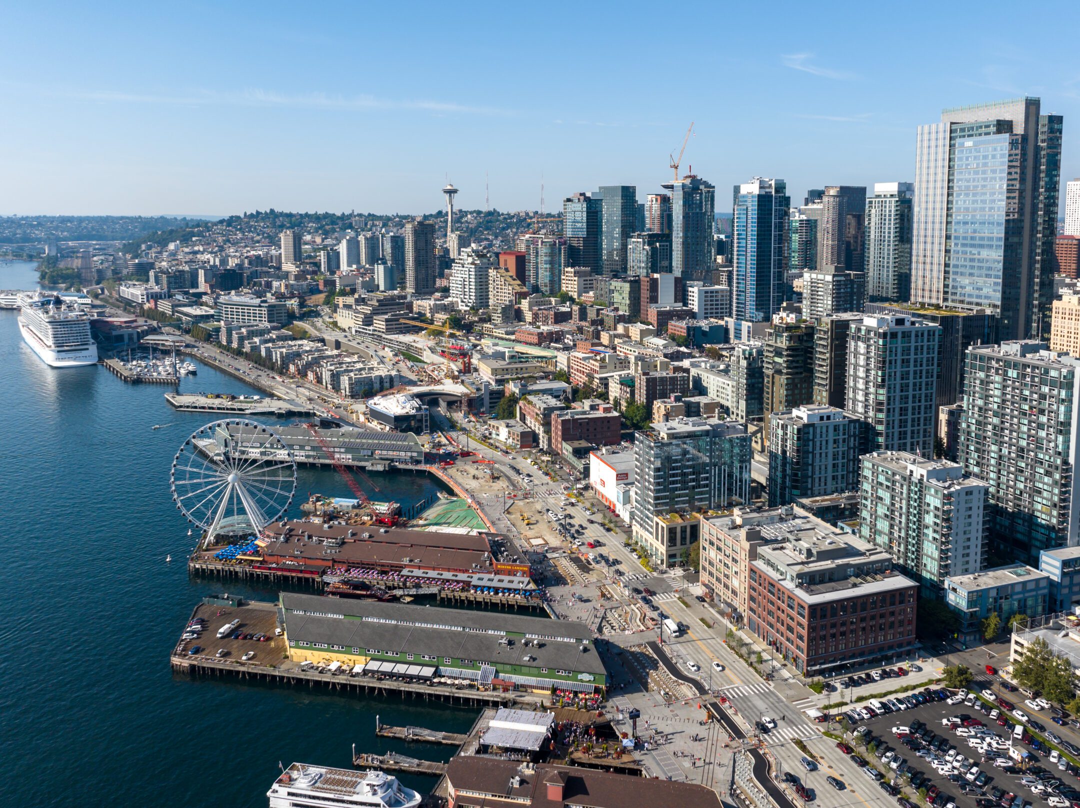 An aerial photograph of the Seattle Waterfront featuring Pier 56, Miner's Landing, and the Seattle Great Wheel on the left, and Downtown Seattle to the right.