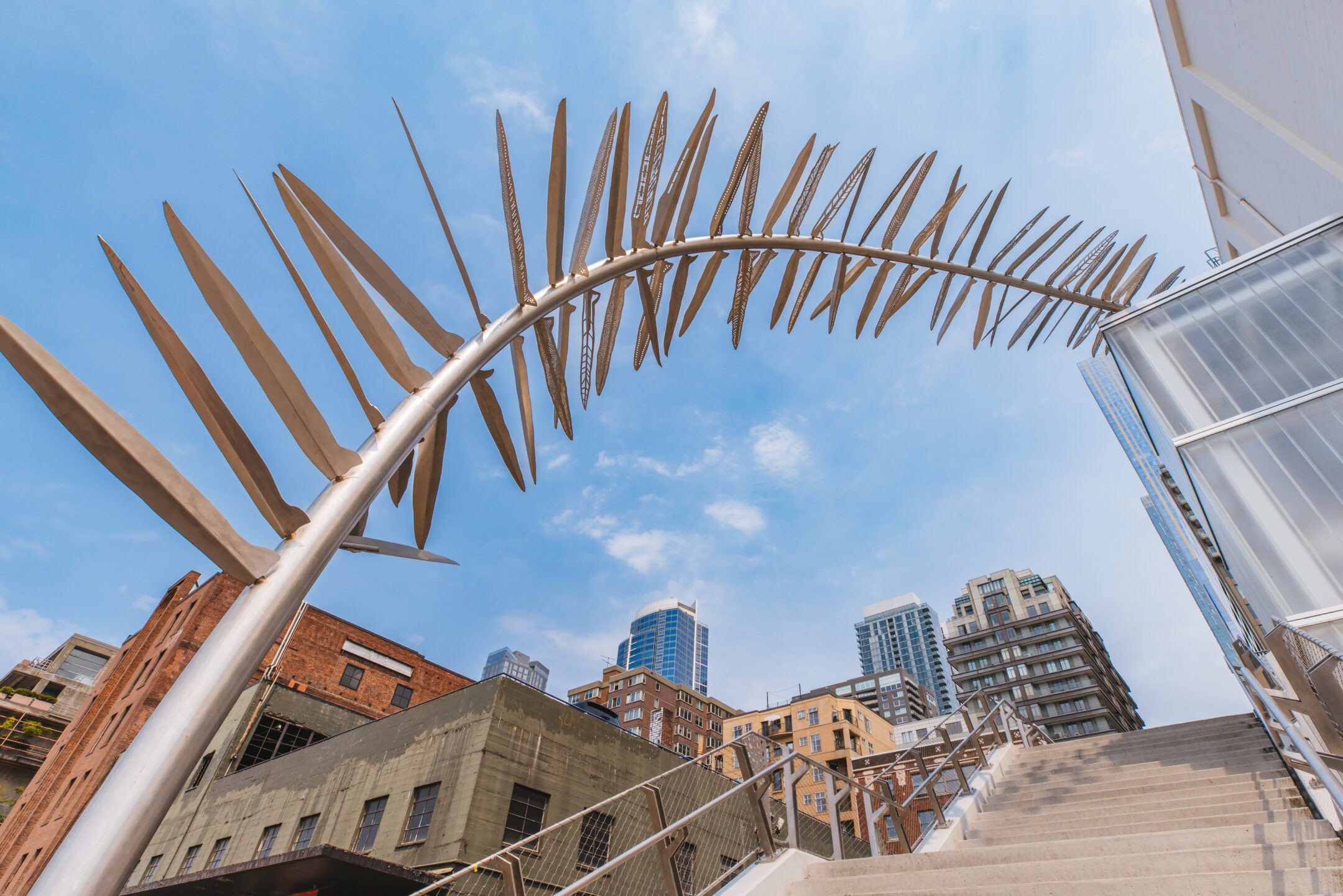 A worm's eye view photo of a fern-like sculpture arching over the Union Street Pedestrian Bridge steps.
