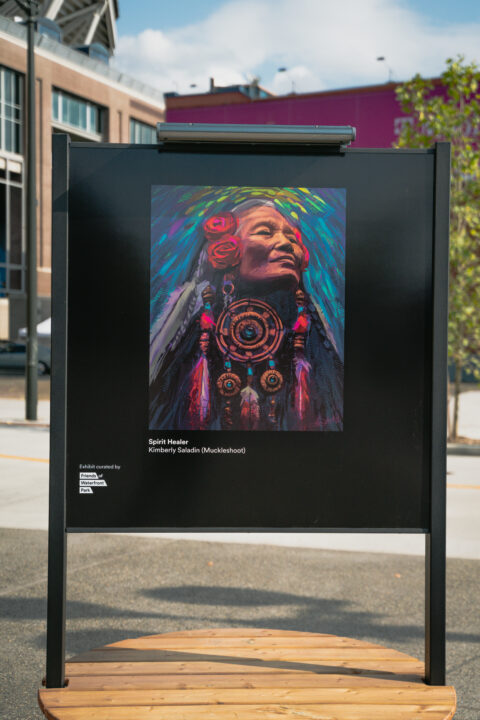 Photo of large art display with digital art of Indigenous woman in vibrant colors and dream catcher, and large feathered earrings.