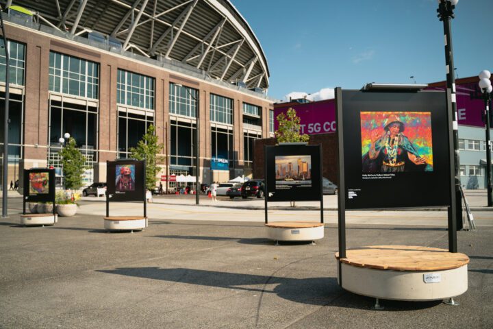 Photo of four large art displays in a plaza with Lumen Stadium in the background.