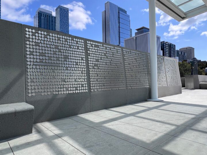 A close-up of the Community Wall at Seattle’s waterfront, featuring rows of metal plaques engraved with names, reflecting the sky and surrounding cityscape.