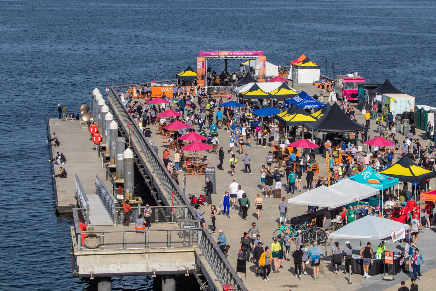Overhead shot of a large gathering of people with pop-up tents and a stage on Pier 62.