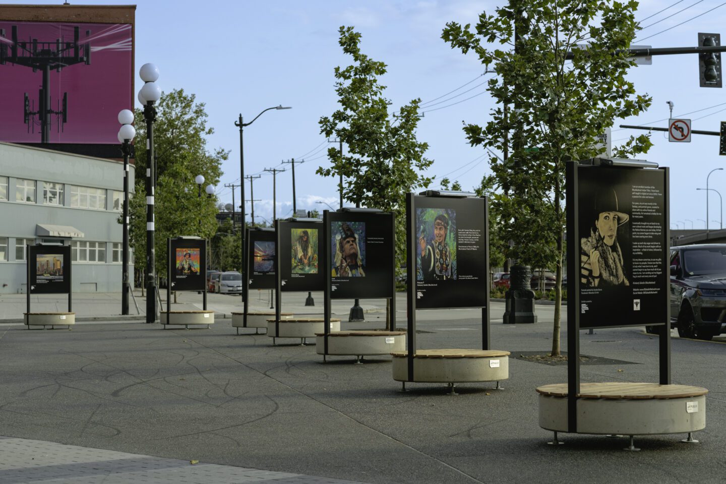 Six free standing art holders in a row in a large open courtyard area.