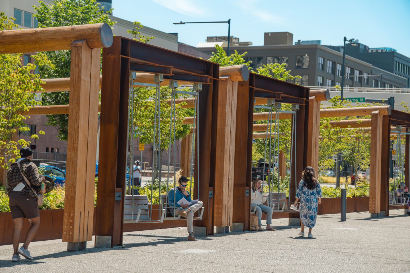 People sitting in large swings and walking by with greenery in the background on the Waterfront Park Promenade.