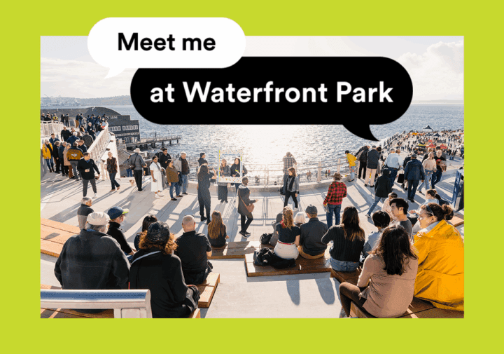 A sunny day at Seattle’s Waterfront Park, where people sit on terraced seating facing Elliott Bay, while others stroll along the promenade. Overlaid speech bubbles read “Meet me at Waterfront Park” on a bright green background.