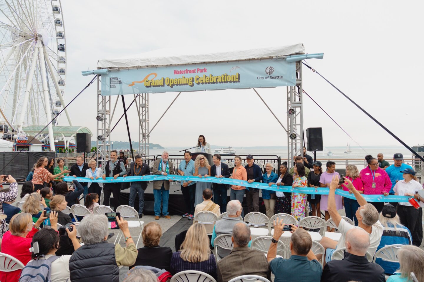 Community members pose in front of stage, preparing for official ribbon cutting.