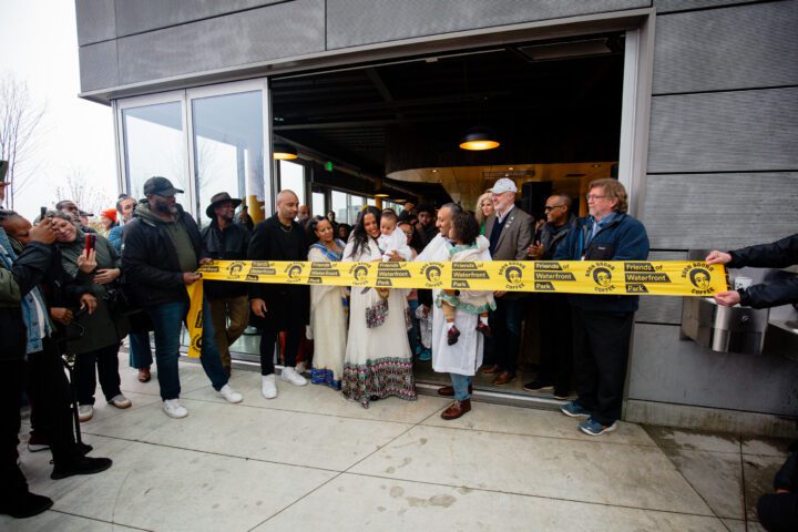 frem holding his child as family, friends and community supporters gather for the official grand opening ribbon cutting.