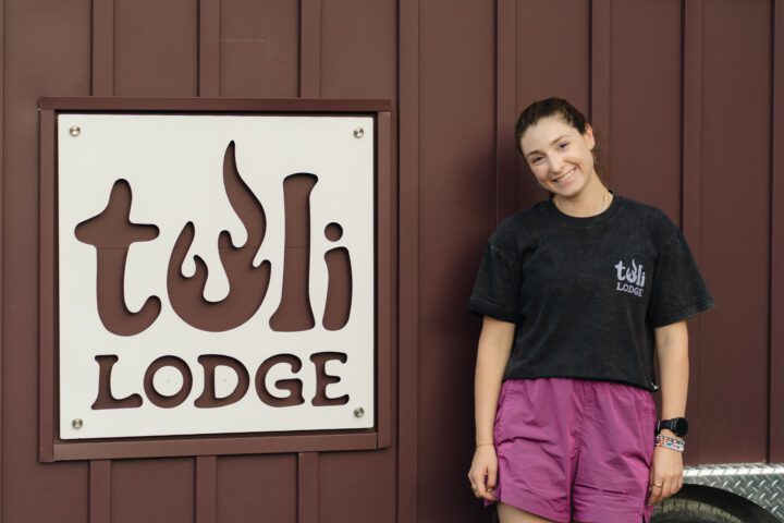 Tuli Lodge founder and CEO Hannah Goldstein posing along sauna cabin with company’s logo.