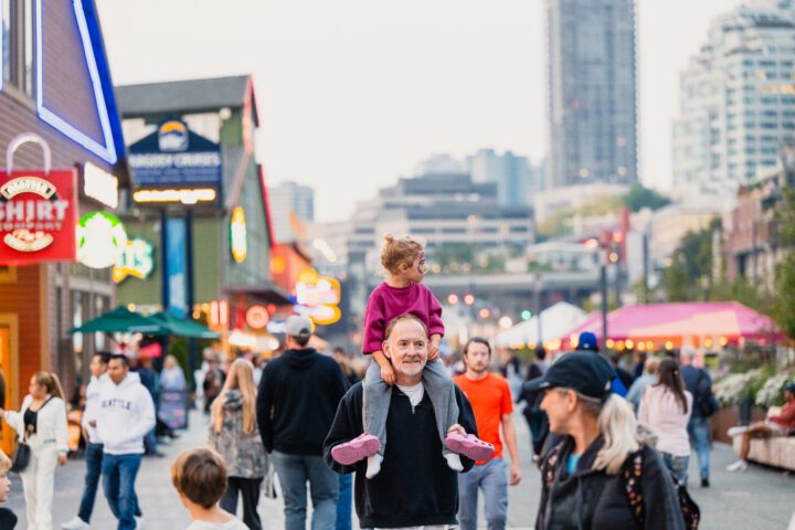 A male person has a small child on shoulders strolling through the Promenade.
