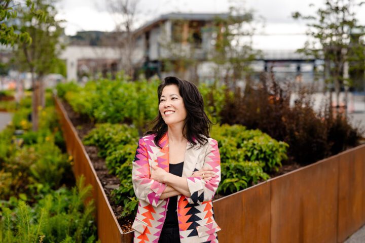 President & CEO Joy Shigaki smiling and posing among native plantings along the Park Promenade.