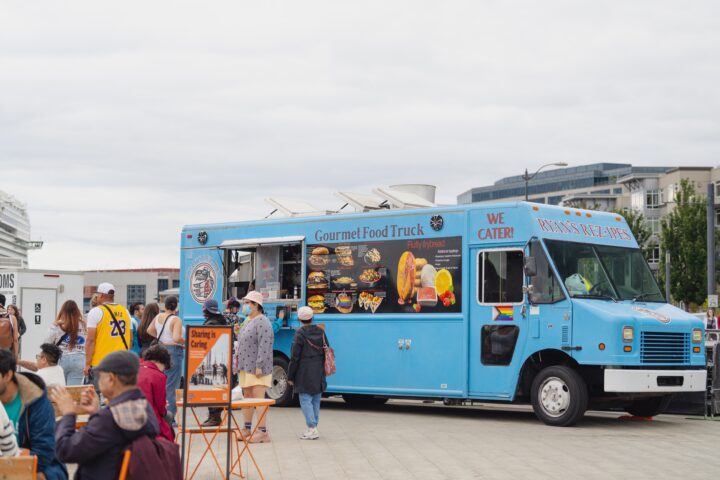 Blue food truck with guests on the left side on a pier
