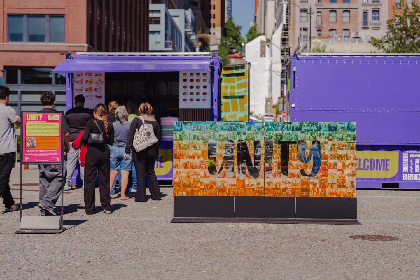 People walking near a large art activation comprised of photos with the word unity in mirror letters.