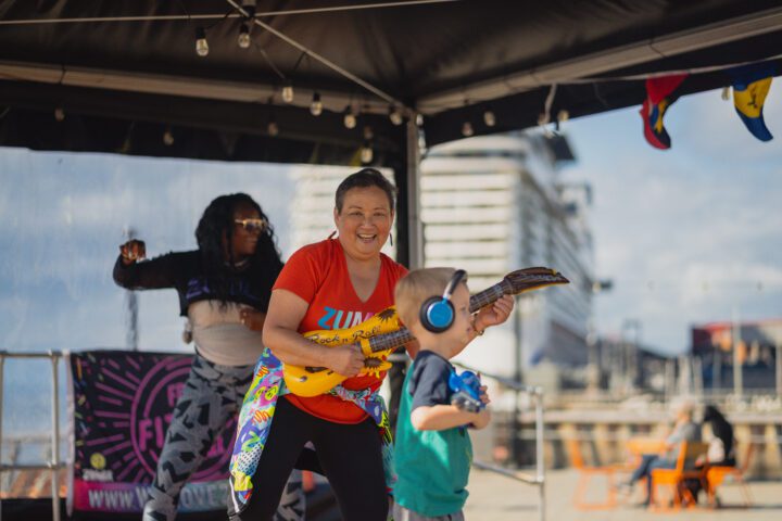 Pure joy on Pier 62 as a We Move to Give instructor Diana Yu with guitar (and Shellone Grant behind them) connects with a young participant during a Zumba class at Waterfront Park. Photo by Jo Cosme.