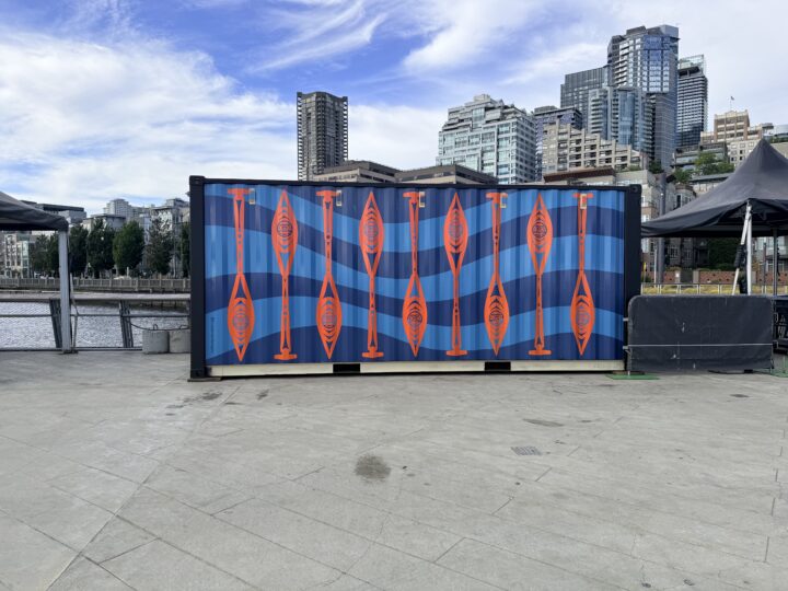 A large shipping container on Pier 62 featuring a repeating pattern of orange canoe paddles against a deep blue wave background — part of Taylor Cameron's Currents of Connection art.