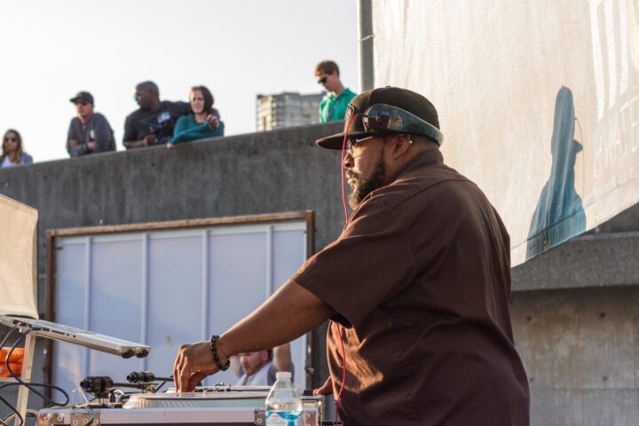 A person standing at a DJ table wearing a hat and headphones.