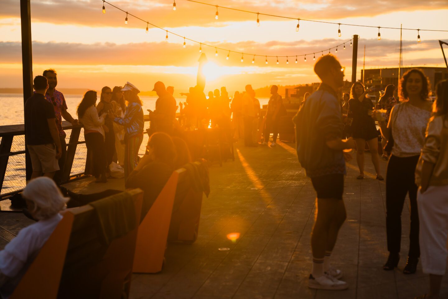 A crowd of people on a pier with the sun setting.