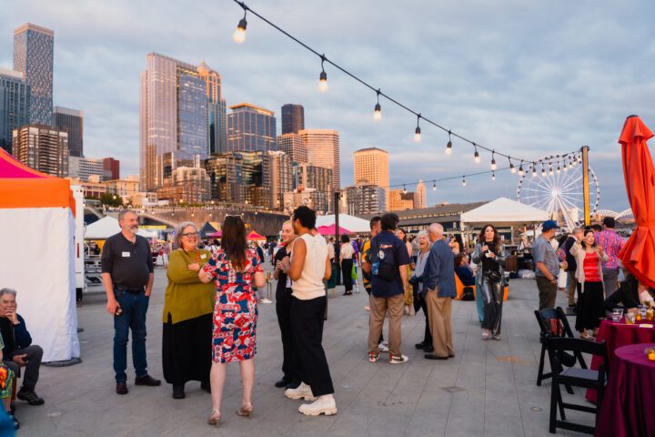 People standing and talking in groups in an outdoor city space.