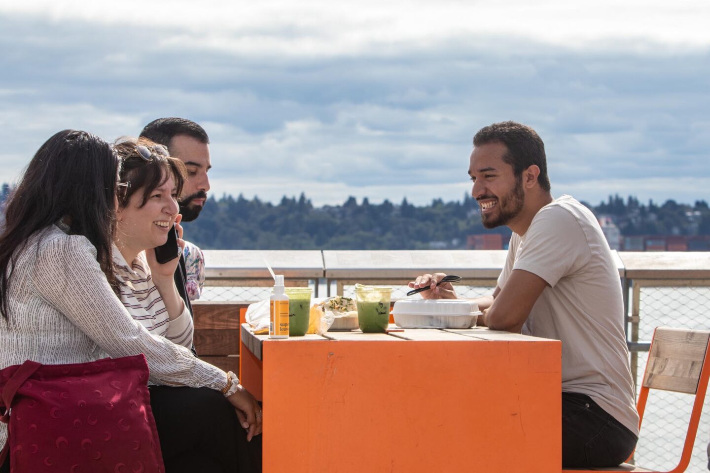Three people sitting at an orange table in front of a body of water.