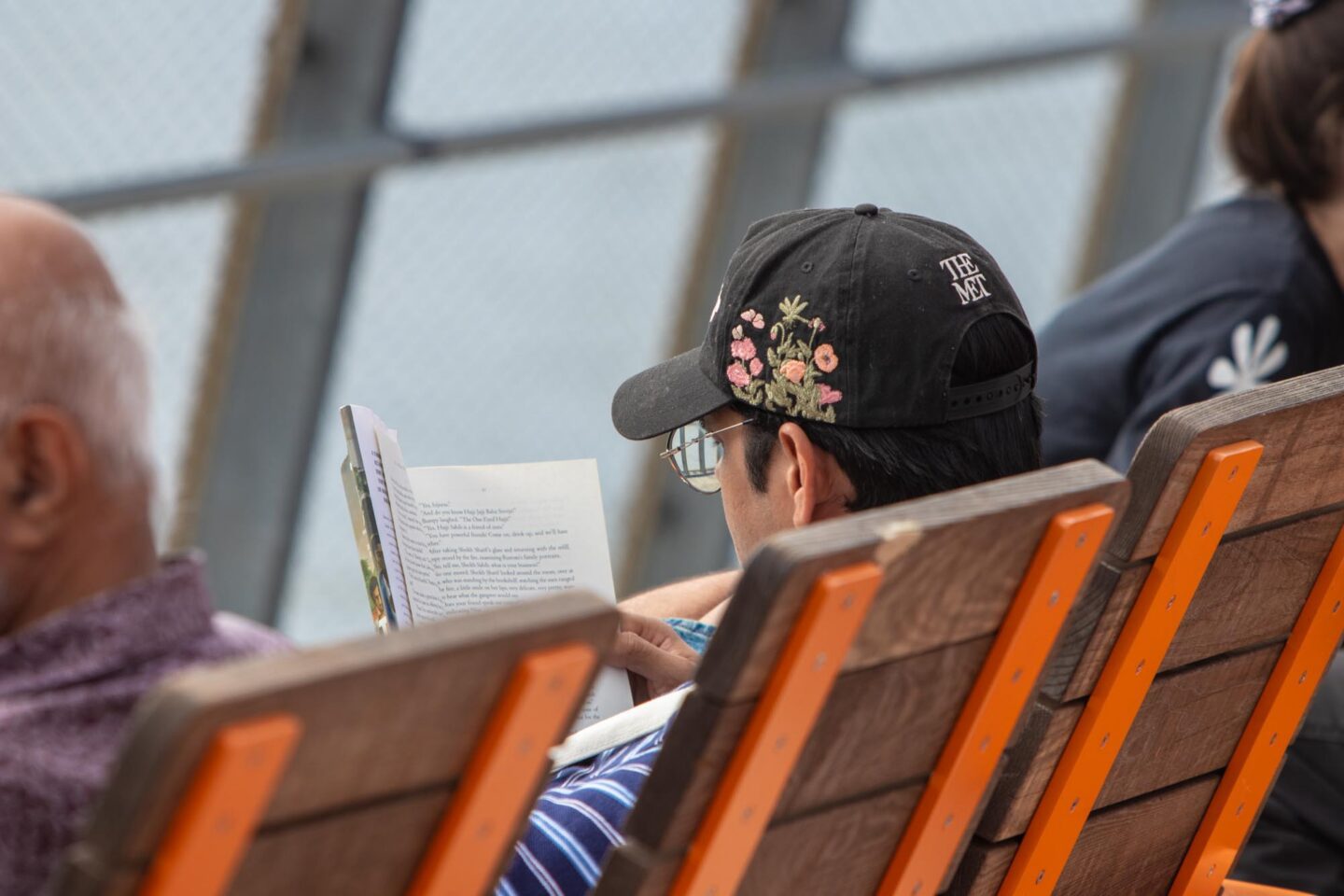 A person wearing glasses and a black hat reading a book.