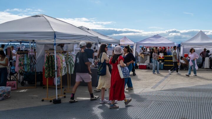 People walking through a large market with vendors under white pop-up tents.