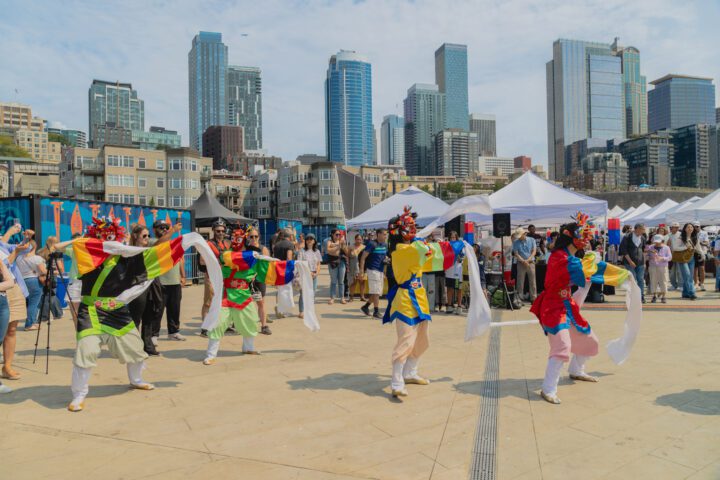 A group of performers in coordinated outfits dancing at a outdoor city event.
