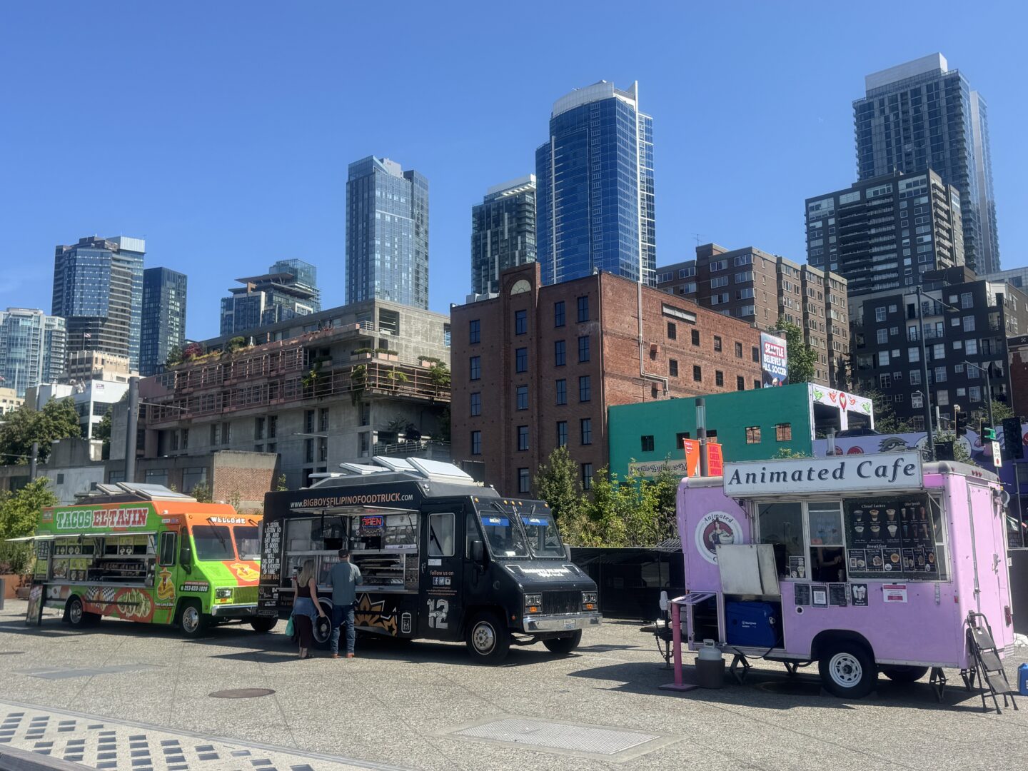 Three food trucks lined up on a city sidewalk.