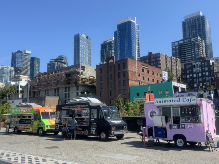 Three food trucks lined up on a city sidewalk.