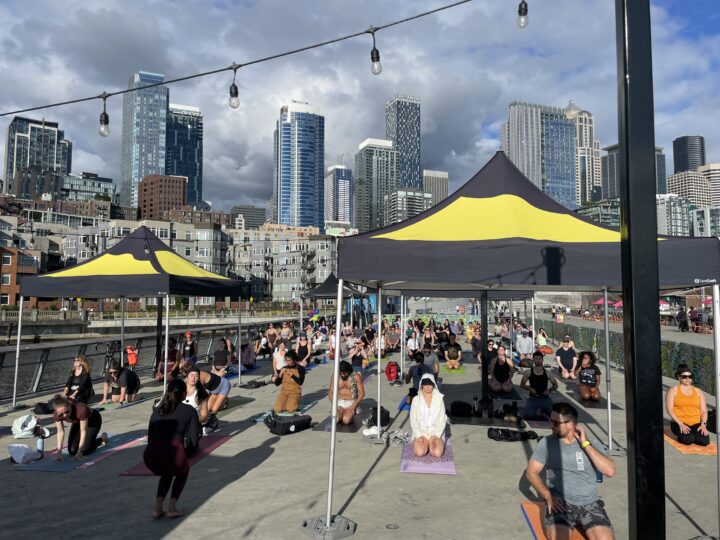 A group of people doing yoga outside on a city pier.