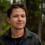 Headshot of Owen Oliver, wearing a flannel shirt and standing outdoors.