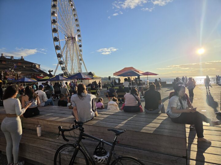 A crowd of people sitting at a performance next to a large ferris wheel.