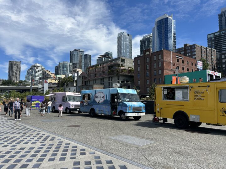 A row of three food trucks lined up on a city sidewalk.